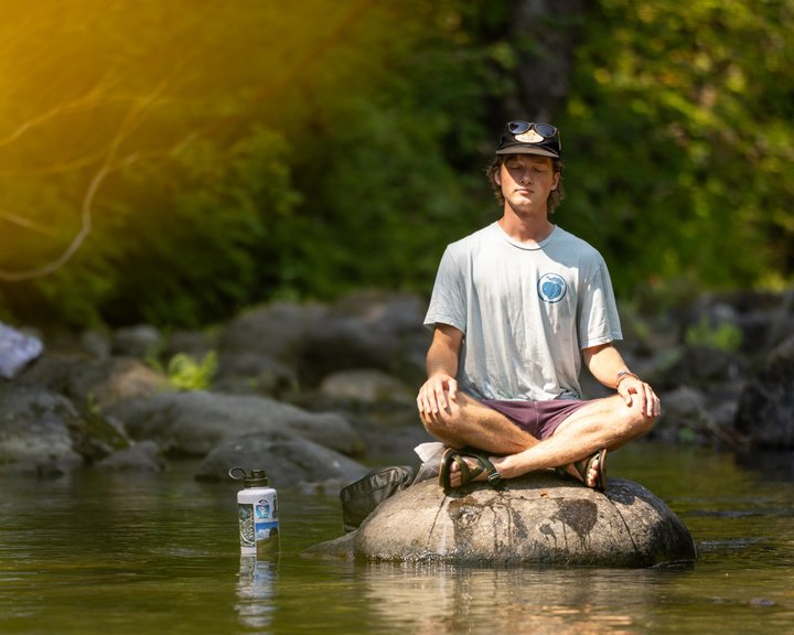 Festival attendee sitting cross-legged on a rock in the river
