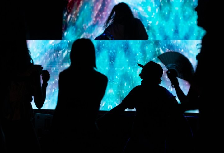 Audience silhouettes in front of a DJ and blue geometric visuals