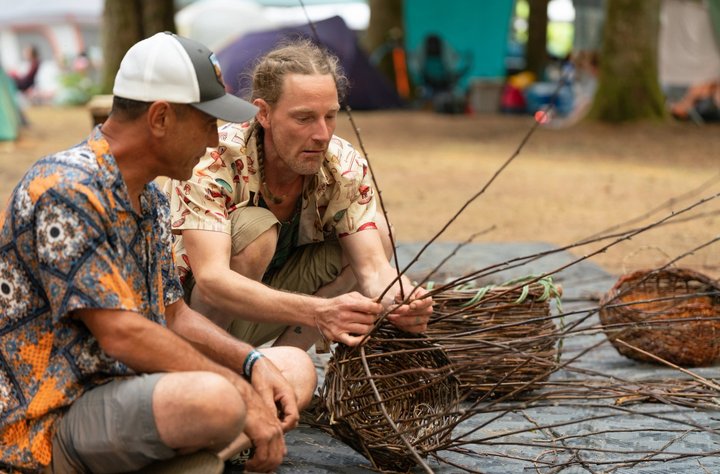 Festival attendees weaving branches into a large basket structure